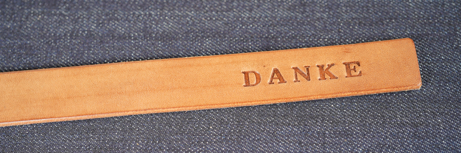 In einen Streifen Leder geprägter DANKE - Schriftzug auf Raw Denim In einen Streifen Leder geprägter DANKE - Schriftzug auf Raw Denim